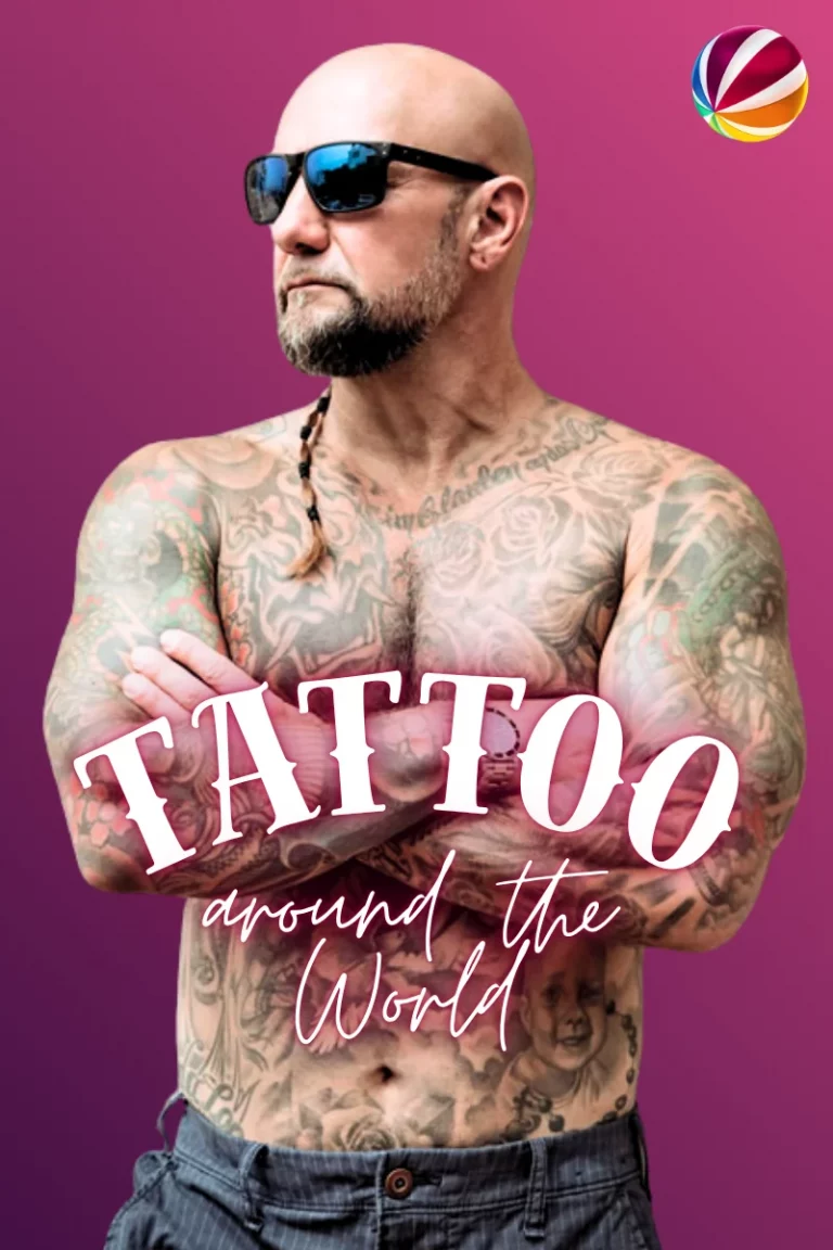 Auf dem Bild sieht man einen von oben bis unten volltätowierten, oberkörperfreien Mann mit Sonnenbrille. Der Kopf scheint bis auf einen kleinen Zopf auf der linken Schulter komplett kahlrasiert zu sein. Er trägt eine Hose mit Nadelstreifen.